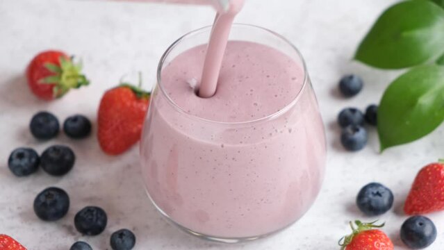 Berry smoothie pouring in a glass. Healthy refreshing cold summer drink, thick pink smoothie