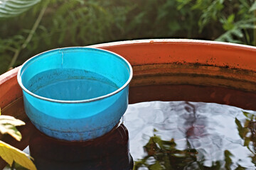 Blue cup on water. Barrel full of water. Plastic barrel used to store water. Bright reflection of the water