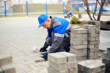 Bricklayer lays paving slabs outside. Working man performs landscaping. Builder lays out sidewalk with stone blocks. Authentic workflow. Hard work in old age.