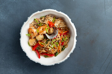 Traditional noodles with seafood in a plate. On a gray background.