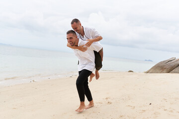 Man piggybacking his gay partner on a beach