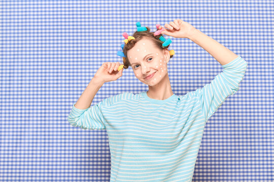 Happy woman with colorful hair curlers, and skincare product on face