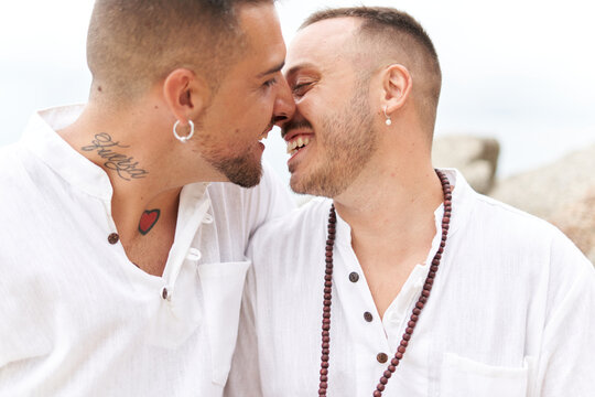 Close up photo of a gay couple smiling tenderly while kissing next to the sea