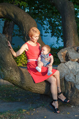 beautiful mother with a son sit on a tree in the park in summer