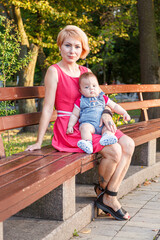 beautiful mother with her daughter and son are sitting on a bench in the park in the summer