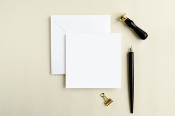 Square card mockup with white envelope, wax seal and calligraphy pen, flat lay with greeting card mock up for design presentation. © IndrePau
