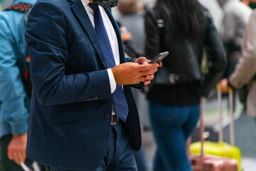 An unidentified man in a blue suit walks and types on his phone while walking with two hands.