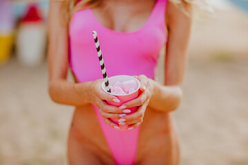 Woman in deep pink bikini with perfect body posing with paper cup of cocktail
