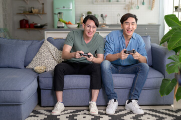 Young smiling gay couple playing video games in the living room at home, LGBTQ and diversity