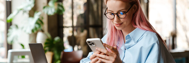 Young woman using laptop and cellphone while sitting in cafe