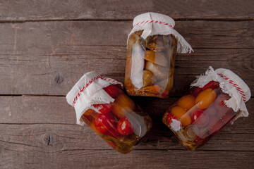 Pickled tomatoes on a wooden table, top view. Seasonal preparation of vegetables in glass bottles. Traditional homemade recipes. Place for text