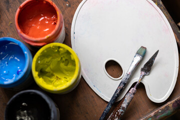 Top view of colored acrylic paint pots, plastic palette, brush and palette knife used for painting in the art studio. Space for copying. Concept of artist and hobby - Powered by Adobe