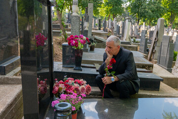 Mature man in black clothes on cemetery, holding a flower and Mourning for family loss. Concept for...