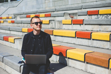 Young businessman working online with a laptop while sitting on a bench outside of his office building