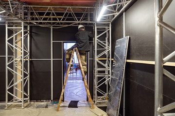 A worker on the stairs carries out the installation of exhibition structures. The builder installs...