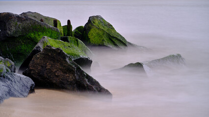 Bright green moss covered black rocks on a Jetty with swirling water in a slow exposure at Sunset Beach in Cape May NJ in the 16:9 format