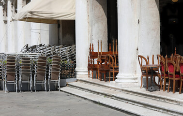 chairs and table of the alfresco cafe piled in the square without people during the economic crisis...