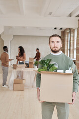 Portrait of serious bearded manager holding cardboard box full of personal stuff while moving into new office
