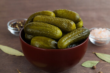 Pickled green cucumbers in a brown bowl with salt and peppers. crunchy Marinated cucumbers gherkins. Salted Cucumbers on a wooden background. Canned vegetables.copy space