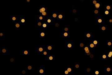 Defocused bokeh lights on black background, an abstract naturally blurred backdrop for Christmas eve or birthday party. Festive light texture. Yellow and red garland in blur. Overlay effect for design