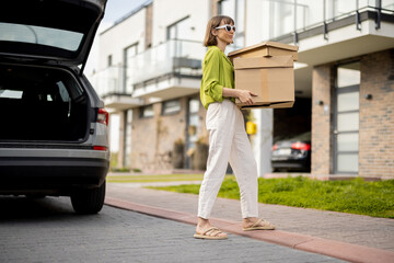 Young woman going home with a parcels, delivering packages by car, vehicle with open trunk on...