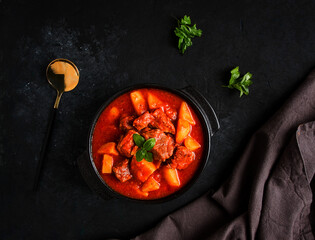 Stew with potatoes, in tomato sauce, with spices and herbs, close-up, no people, on a black background