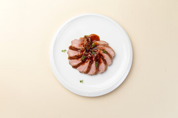 Fried duck fillet cut into slices and sauce in a plate.
