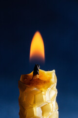 a yellow candle with a honeycomb texture burns on a dark background
