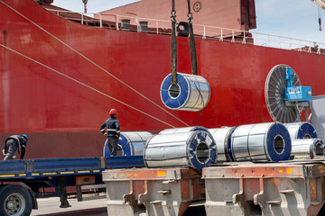 Packaged coils, galvanized steel and large tin rolls are loaded onto the ship by crane from...