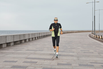 Active senior man in sportswear and sunglasses jogging in the morning along seaside horizontal shot