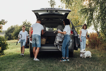 Four Members Family Traveling by Minivan Car, Mother and Father with Two Teenage Children and Pet West Highland White Terrier Dog Having Picnic Outdoors