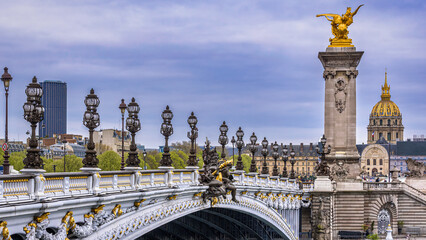 De sierlijke Pont Alexandre III in het centrum van Parijs, Frankrijk met de gouden koepel van de Invalides en de Tour Montparnasse op de achtergrond onder een bewolkte hemel