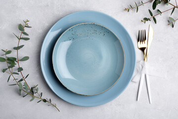 Festive table setting with blue ceramic plate, golden cutlery set and fresh eucalyptus leaves on...