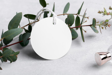 Round white gift tag mockup with eucalyptus leaves on grey background, label tag mockup, Wedding favor tag for souvenir, sign for greeting message close up, element for design