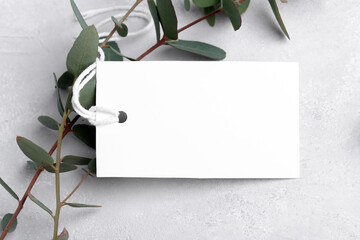 Rectangle white gift tag mockup with eucalyptus leaves on grey background, label tag mockup, Wedding favor tag for souvenir, sign for greeting message close up, element for design, close up