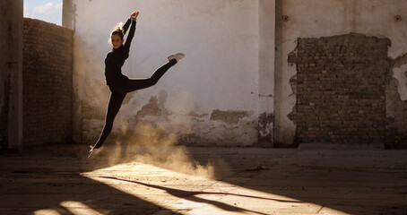 Ballerina jumping and dancing in a dusty abandoned building on a sunny day