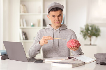 Male medical student sitting with a laptop computer and holding a brain model