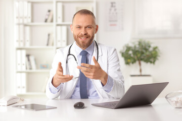 Doctor sitting in an office with a laptop computer and explaining by gesturing with hands