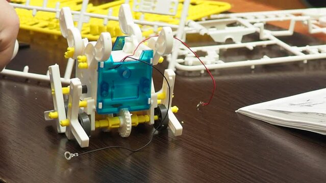 young male constructor scientist assemble the wheeled machine robot in the lab. boy teenager collects according to instructions robot constructor. connects wires, programs. develops intelligence.