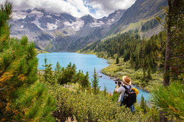 landscape photographer with dslr camera in beautiful wild nature, standing with backpack on top of mountain