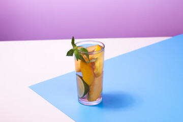 Refreshing summer drink. Peach juice or cocktail with peach slice, ice cube and mint on abstract geometrical white, blue and pink background.