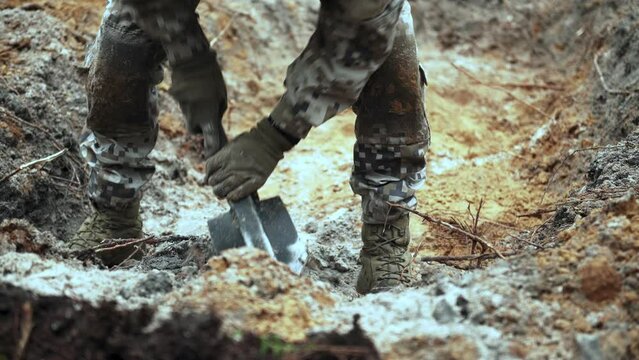 One soldier digs a trench in a pine forest. Close-up of a shovel and sand.