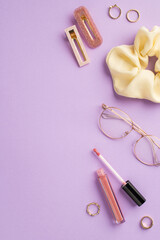 Makeup beauty concept. Top view vertical photo of stylish glasses scrunchy pink lip gloss gold rings and barrettes on isolated pastel violet background