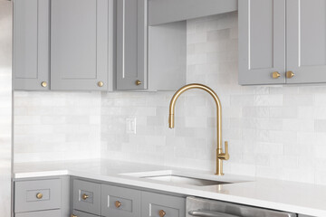 A kitchen sink detail shot with a gold faucet, marble backsplash, grey cabinets, and gold hardware. - obrazy, fototapety, plakaty