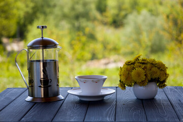 Teapot with tea and dandelion flowers. Tea in nature. Blurred background.