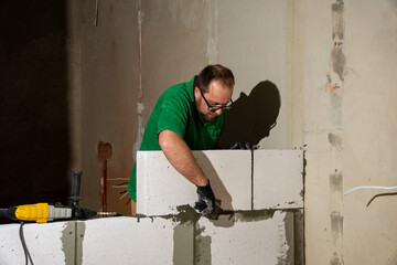 Builder laying a wall of gas blocks with tools and adhesive mortar.  Construction from ACC blocks. A worker builds an inner wall of a house from aerated concrete bricks.