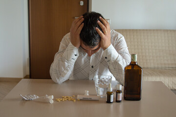 Desperate man with test tubes in hand, with the table full of medicines such as anxiolytics,...