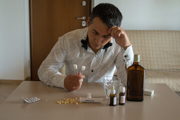 Desperate man with test tubes in hand, with the table full of medicines such as anxiolytics,...