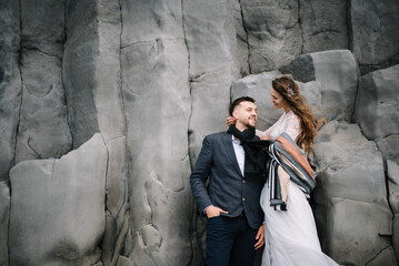 Wedding in Iceland. A young guy and a girl in a white dress astanding on the ledges of the rock
