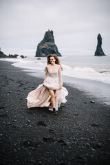 Bride in old classy wedding dress are running on the Black Sand beach in Vic, Iceland with rock islands on background.
